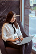 © valeriyakozoriz - elegant woman on white jacket is sitting on armchair in office and working on a laptop, notebook