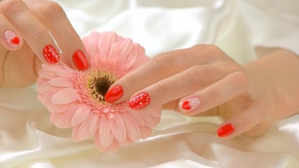 Wall Mural - Delicate hands with flower, slow motion. Young woman hands with beautiful manicure gently touching gerbera on white silk. Tenderness and care concept.