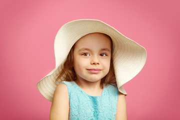 Wall Mural - Little beautiful girl in beach hat and blue dress on pink isolated background.