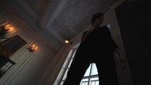 A Woman With A Short Haircut In A Black Pantsuit, With A Jacket On The Naked Body Goes To The Camera, Shooting From The Bottom Point To Full Height. In The Interior Of The Loft In Front Of A Large Win