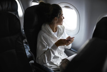 Woman With Smartphone Sits On Black Seat In Plane