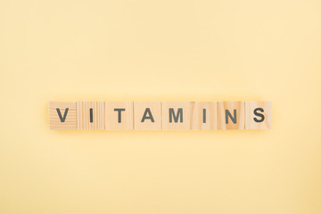 Wall Mural - top view of vitamins lettering made of wooden cubes on yellow background