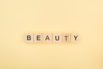Wall Mural - top view of beauty lettering made of wooden cubes on yellow background