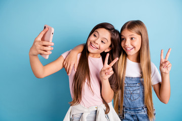 Sticker - Close up photo two little she her blond brunette girls long pretty hair telephone make take selfies for mom mommy show v-sign wearing casual jeans denim t-shirts isolated blue bright background