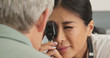 Close up on doctor using ophthalmoscope to look into eyes of senior male patient. Japanese woman primary care physician or ophthalmologist doing check up