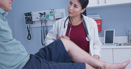 Wall Mural - Patient with hurt knee getting it checked by female medical professional. Physical therapist or doctor with older male patient in exam room checking range of motion on knee injury