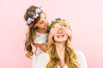 Wall Mural - cute child standing behind smiling mother and closes her eyes with hands on pink background