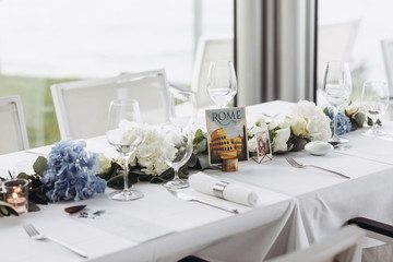 Wedding table decoration. Floral garland of greenery and blue flowers lies between glasses on the white table