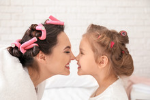Portrait Of Young Mother With Cute Little Daughter With Hair Curlers At Home