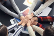 © Pixel-Shot - Group of people putting hands together as symbol of unity in office