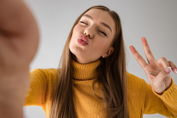 Wall Mural - Happy young woman isolated over grey wall background take a selfie by camera.