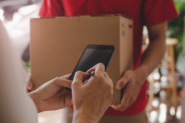 home delivery service man in red uniform and young woman customer appending signature in digital mob