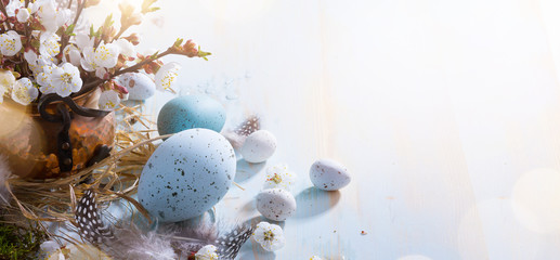 Wall Mural - bright easter background; easter eggs basket and sprig flowers on blue table background