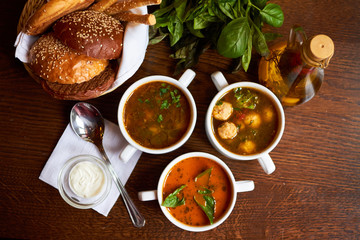 Wall Mural - soups menu. 3 types of soups on a wooden table with a bread basket, spices, olive oil, a spoon and a white sauce