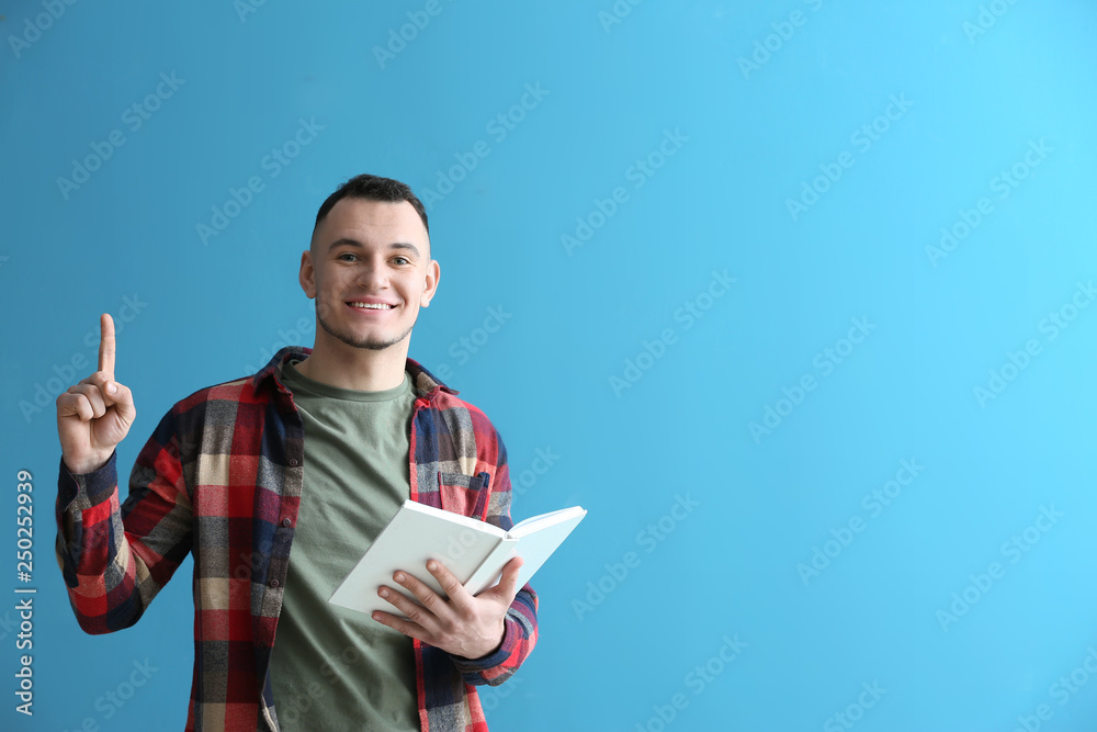 Handsome young man with book and raised index finger on color background