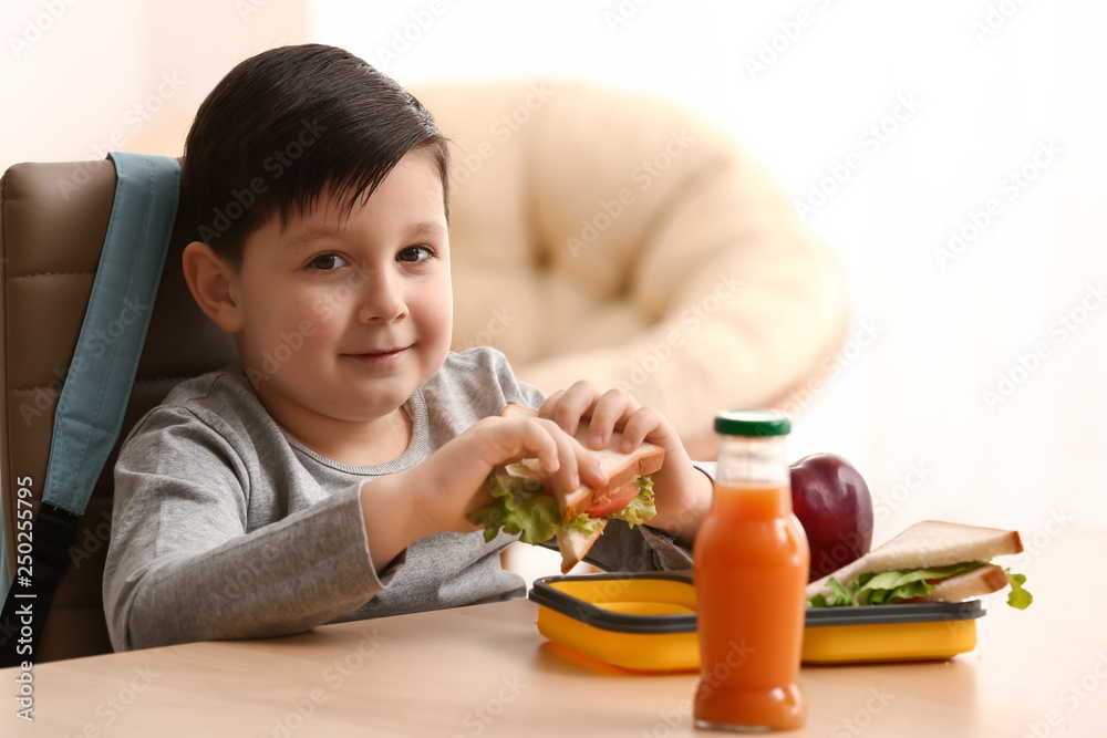 Little schoolboy eating tasty lunch at home