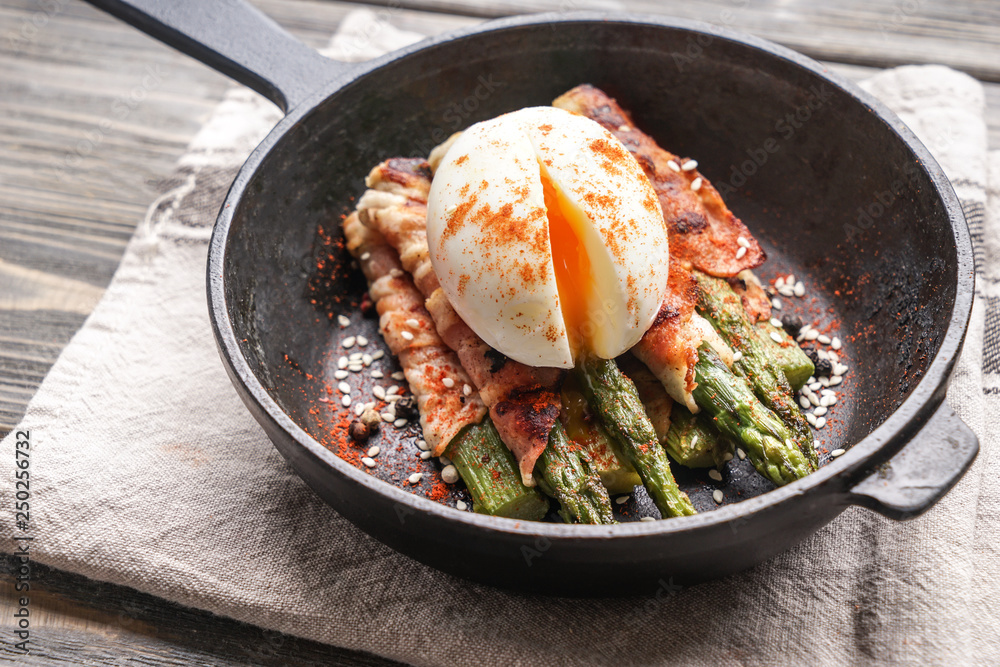 Frying pan with tasty bacon wrapped asparagus and egg on table