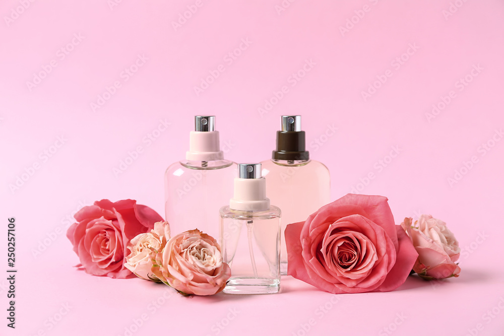 Bottles of perfume and flowers on color background