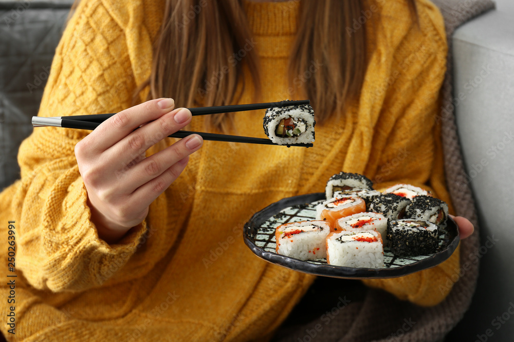 Woman eating tasty sushi rolls at home