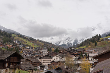 Alpine village with high bell tower on the background of the Alps