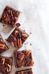 Wall Mural - homemade chocolate fudge brownies with pecan nut and dried cranberry on white baking paper background.