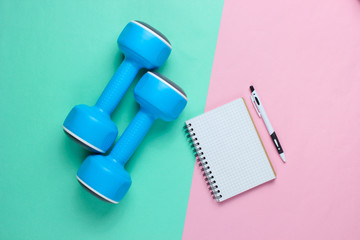 Fitness concept, workout plan. Plastic blue dumbbells, notepad on  pastel background. Top view. Flat lay