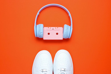 Wall Mural - Retro style. 80s. Pop culture. Minimalismalism. Headphones with audio cassette, white sneakers on   orange background. Top view