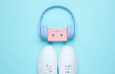 Wall Mural - Retro style. 80s. Pop culture. Minimalismalism. Headphones with audio cassette, white sneakers on blue  background. Top view