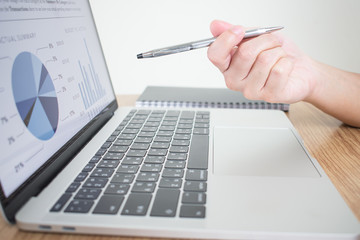 Poster - The close-up image of a businessman pointing to the laptop screen to explain the financial graph on the desk.