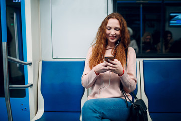 Wall Mural - Positive redhead young female with mobile phone in subway train