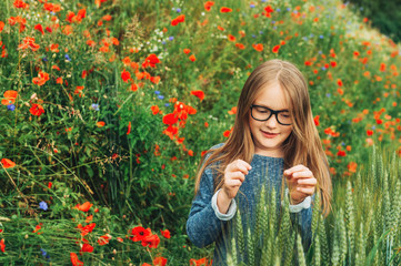 Outdoor portrait of adorable little blond girl of 8-9 years old in poppy field, wearing eyeglasses