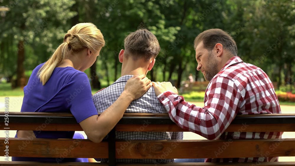 Caring mother and dad supporting sad teen son sitting on bench in park, crisis - obrazy, fototapety, plakaty 