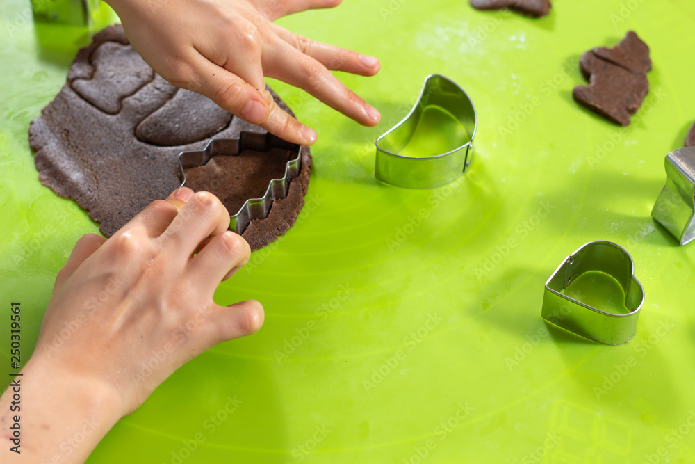 Dłonie chłopca wyciskającego kształty z metalowych foremek z ciasta położonego na zielonej silikonowej stolnicy. Zajęcia kulinarne dla dzieci. - obrazy, fototapety, plakaty 