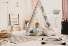 Cute Child Reading A Book, Laying On The Pillows In Stylish Scandinavian Tent In Playroom