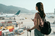 © PR Image Factory - young girl seeing view of busy airplanes apron standing near window holding cellphone backpack and luggage in hall walking to lounge area. travel woman search online map in hong kong airport to gate