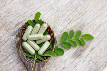 Herbal capsules with herb leaf on wooden table 