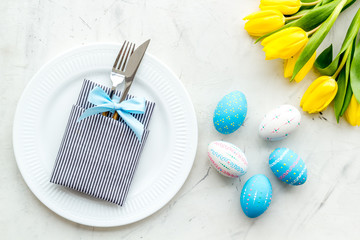 Festive traditional Easter dinner concept. Tableware, painted eggs, tulips flowers on white stone table top view