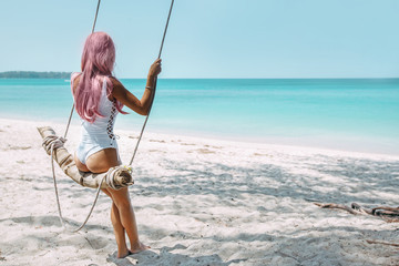 Wall Mural - Girl with pink hair hanging on swing at beach