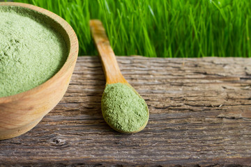 Young barley and chlorella spirulina on wooden board and green grass