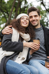 Canvas Print - Portrait of european people man and woman 20s drinking takeaway coffee from paper cups, while sitting on bench in green park