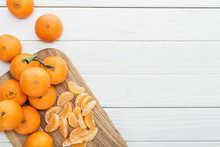 Top View Of Peeled Tangerine Slices And Whole Ripe Tangerines On Wooden Chopping Board