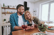 © Yakobchuk Olena - Cheerful happy couple using smartphones and having dinner at home