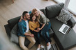 © Yakobchuk Olena - Happy parents hugging their daughter while sitting on couch with laptop