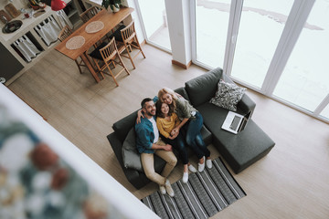 Wall Mural - Happy parents sitting on couch with laptop and hugging their daughter