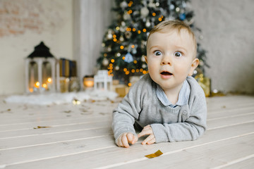 Adorable little boy looks happy lying on the floor with toys before a Christmas tree