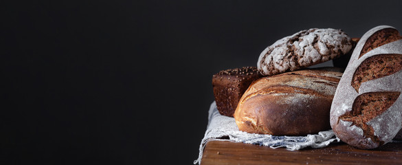 Loafs Of Traditional And Natural Bread on a wooden table with linen towel. Assortment of artisanal bread. Healthy food concept. Panoramic frame with free space for input text.