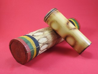 Close-up of two “ganzás”, a Brazilian rattle used as a percussion instrument, especially in samba music. They are handmade and made of bamboo. Pink background.