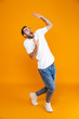 © Drobot Dean - Full length image of frightened guy 30s in t-shirt and jeans raising hands while standing, isolated over yellow background