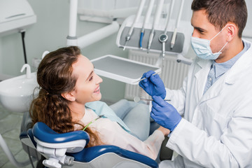 Wall Mural - dentist in mask and latex gloves standing near smiling woman in dental clinic