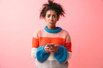 Poster - Sad beautiful young african woman posing isolated over pink wall background using mobile phone.